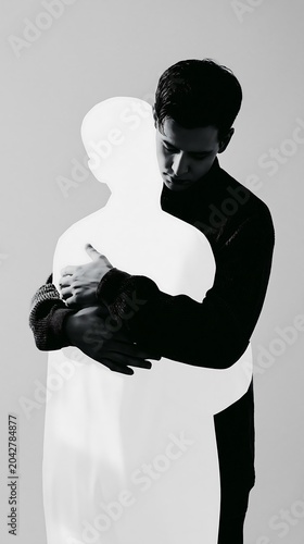 Conceptual black and white photography of a young man embracing an empty glowing silhouette representing loneliness and self love