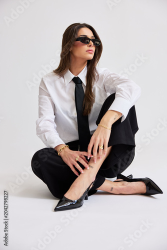 Woman in black and white outfit sits on floor with sunglasses