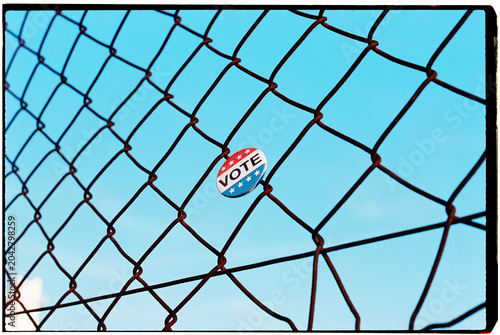 a vote badge is caught in a wire fence against a blue sky, 35mm film