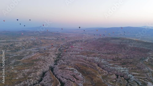 Goreme, Nevsehir, Turkey. Mass fleet of hot air balloons with visible fire bursts drifting over Red Valley at sunrise, aerial panoramic view over eroded rock formations. Aerial View