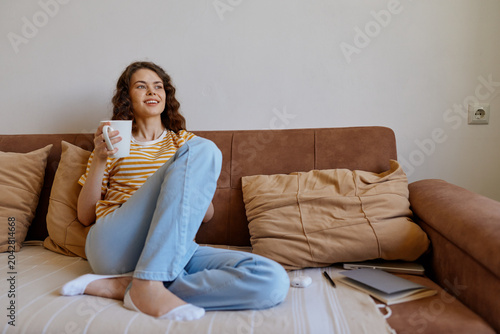 Canvas Print Cheerful woman home lifestyle on a couch, sipping from a mug, casual striped top
