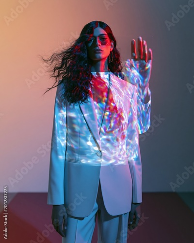 Sophisticated woman in a light suit posing with holographic light projections across her body for future technology, high fashion editorial and corporate advertising