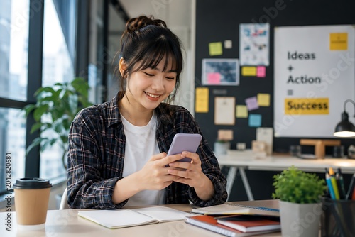 Young smiling woman working on smartphone at modern desk in creative office environment with colorful posters