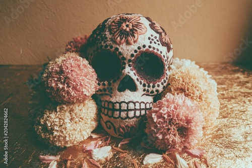 Decorative sugar skull with marigold flowers sits on a golden surface for cultural celebration, festive advertising and holiday marketing with copy space on the side