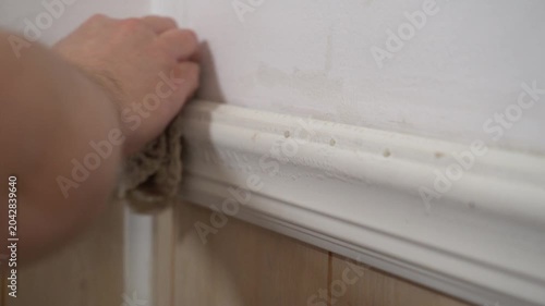 Man wipes, cleans a dirty white wall with a white towel. Household chores. Cleaning your home. Spring cleaning.