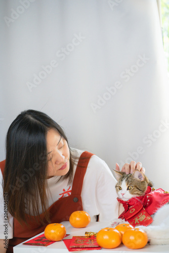 chinese new year concept with asian woman play with cat wearing red chinese traditional cloth with red envelope orange and gold on table