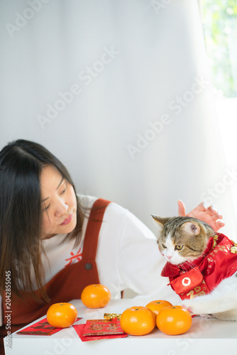 chinese new year concept with asian woman play with cat wearing red chinese traditional cloth with red envelope orange and gold on table