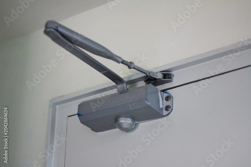 Fotografie Close-up of a grey hydraulic automatic door closer arm mechanism installed on a white door
