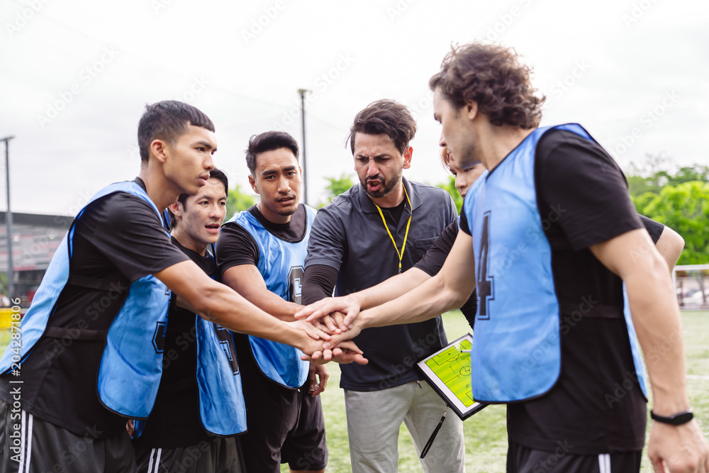 Naklejka premium Soccer team and coach stacking hands to unify and motivate before a match. Teamwork, shared goal, and professional leadership concept in sports.