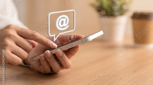 Hands using a smartphone with virtual speech bubbles containing email and hashtag symbols. Concept of social media communication and digital marketing