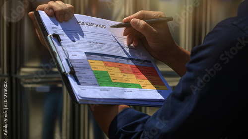 Focused worker conducts serious maintenance risk review holding clipboard with safety chart and pen during careful industrial inspection