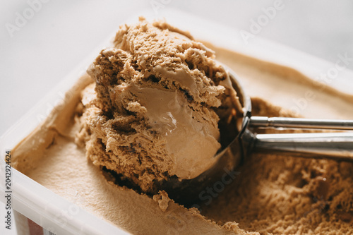 Scooping fresh coffee ice cream from a plastic tub container.Close-up of homemade chocolate ice cream with a metal scoop.Delicious creamy mocha ice cream texture in a tub, side view.dessert for hot da