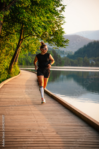 Woman running by the lake on a sunny day. Active lifestyle and outdoor fitness concept.