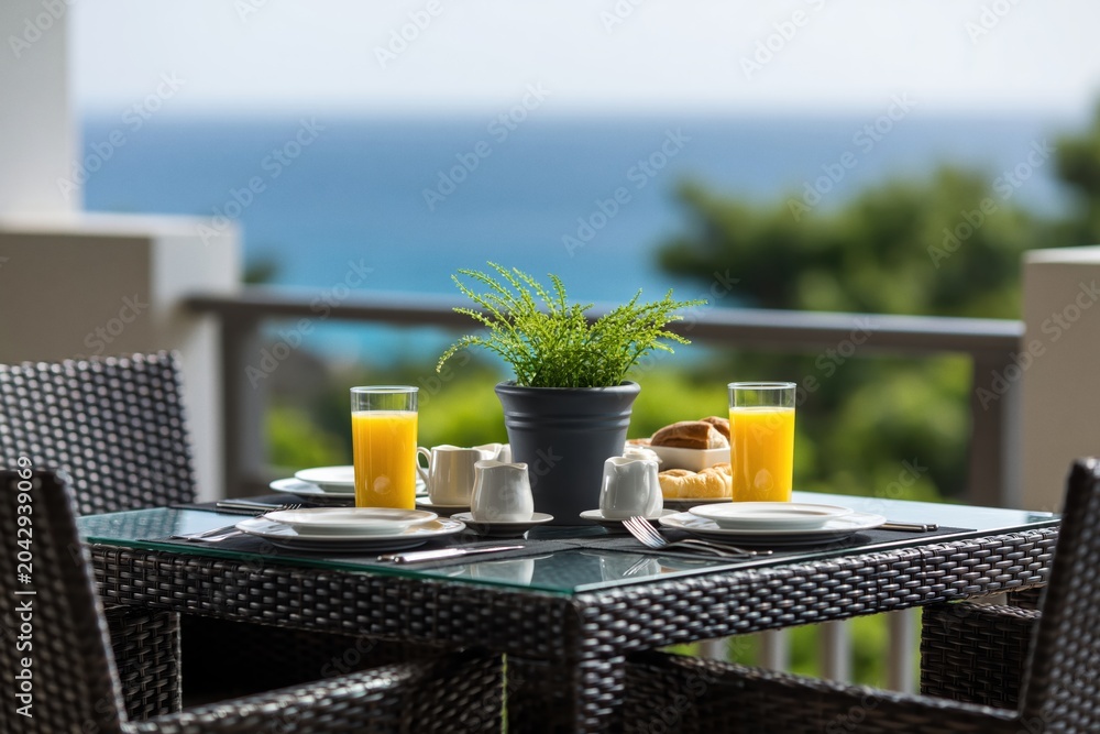 Fototapeta premium Breakfast on balcony with ocean view table chairs wicker furniture juice