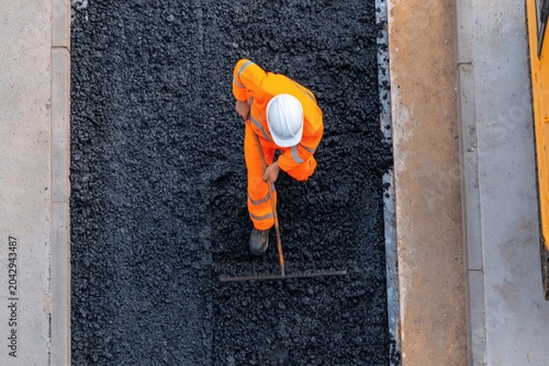 Construction worker leveling fresh asphalt for road paving and highway maintenance