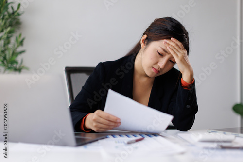 Obraz na plátně Asian businesswoman holding a document, suffering from a headache and work stres