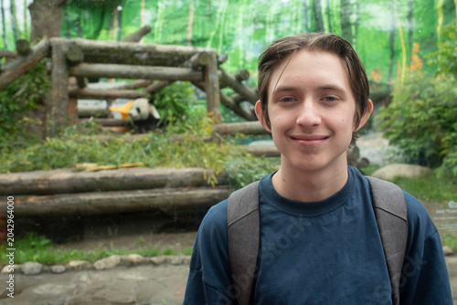 Teenage tourist boy smiling near giant panda enclosure at Moscow Zoo in Russia