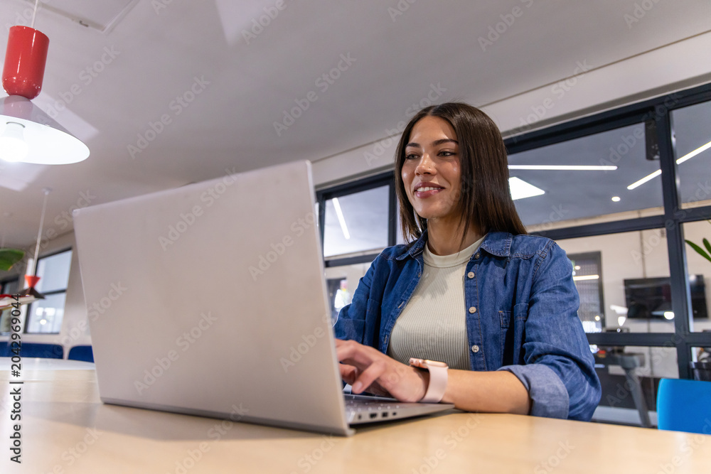© wavebreak3 - Adult woman with smartwatch working on silver laptop at light-wood table in open office, copy space