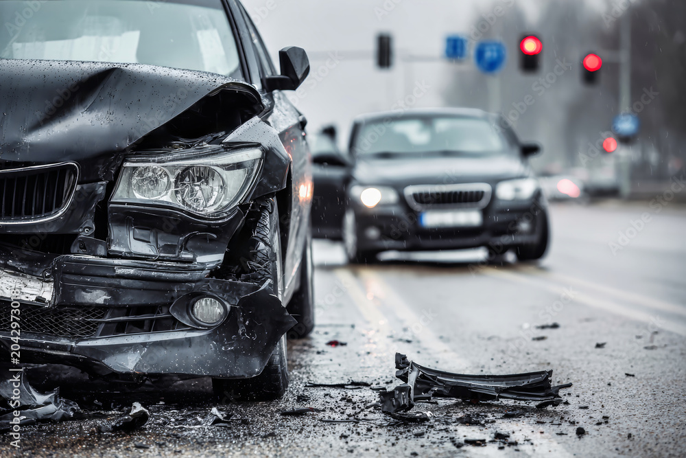 Fototapeta premium Two cars are involved in a collision on a city street. One vehicle is damaged, while the other is stopped at a red light. Rain is falling