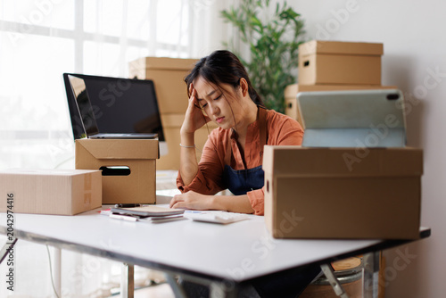 Fényképezés Young asian woman at home office desk looks exhausted and overwhelmed, holding h