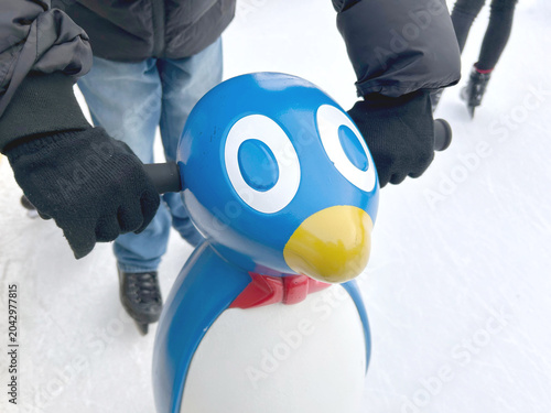 Child holding a penguin-shaped skating support while learning on an ice rink