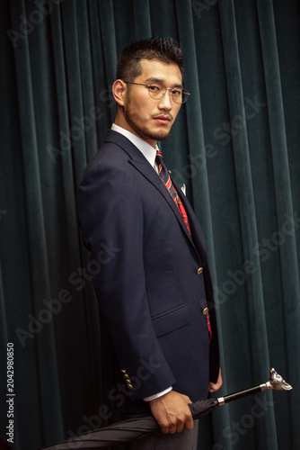 Fotografía Elegant suited man holding decorative cane against velvet curtain