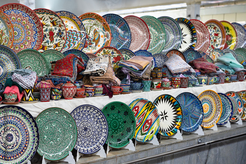 Colorful hand-painted Uzbek ceramic plates and cups displayed at Siab bazaar in Samarkand. Traditional pottery and textiles make a vibrant market stall, ideal for travel and cultural content.