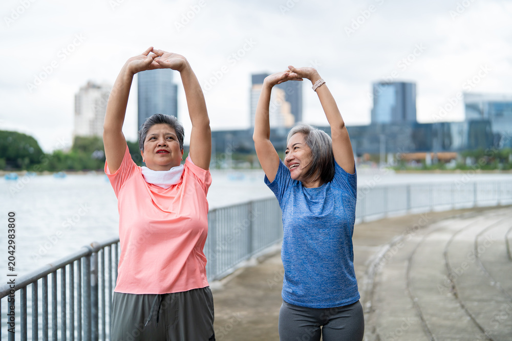 Obraz premium Two Asian senior women warm up body and exercise outdoor in modern city. 