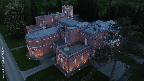 Aerial view of Chateau Mukhrani royal palace and estate in Georgia, magnificent pink castle architecture with a tower surrounded by a lush green park, gardens and pathways on a spring day.