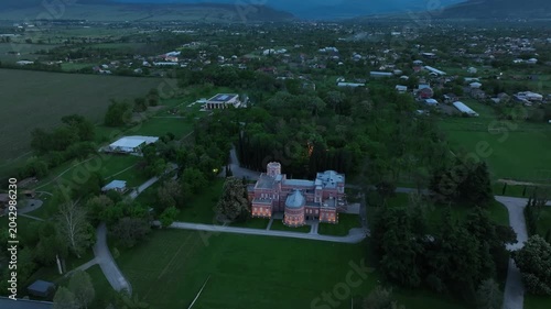 Aerial view of Chateau Mukhrani royal palace and estate in Georgia, magnificent pink castle architecture with a tower surrounded by a lush green park, gardens and pathways on a spring day.