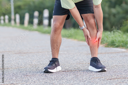 Foto Athletic man having leg ache and shin pain while jogging in the park