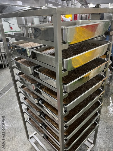 Stainless steel trays containing work-in-process food products arranged on a mobile rack trolley in a food manufacturing facility. Material handling and temporary storage system supporting efficient p