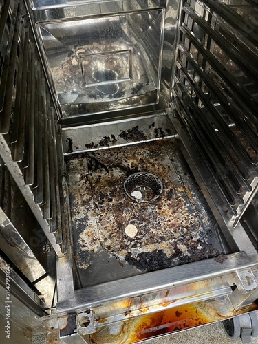 Commercial food processing oven requiring hygiene inspection after cleaning. Visible food residue and cleaning material remnants highlighting sanitation verification and equipment cleanliness monitori