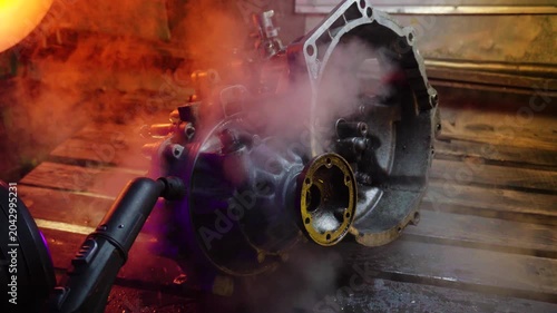 cleaning and washing with a steam cleaner of an old manual transmission from a front-wheel drive car for repair evening video shooting with red and purple lighting