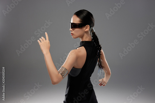 Futuristic woman in visor sunglasses raising hand in studio