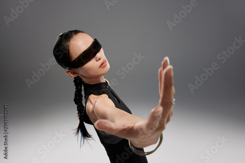 Futuristic woman in black dress with smart glasses reaching forward in studio