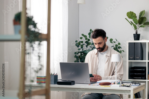 Canvas Print Young man concentrating on laptop and smartphone at desk