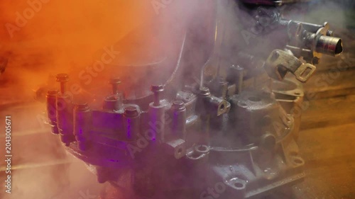 cleaning and washing with a steam cleaner of an old manual transmission from a front-wheel drive car for repair evening video shooting with red and purple lighting