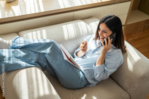 Konstfotografi Woman relaxing on sofa talking on smart phone