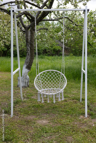 White Garden Swing Among Lush Green Trees and Summer Foliage