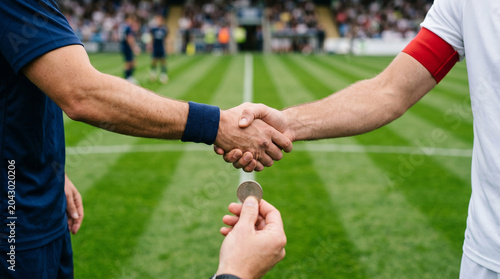 Close up of soccer team captains shaking hands before match with referee holding coin
