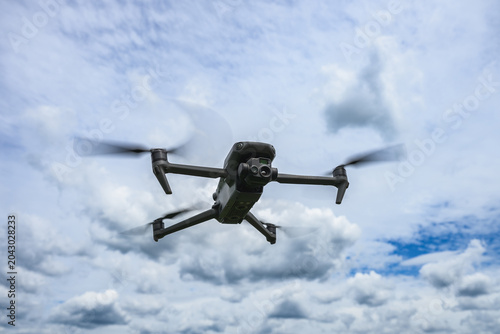 Modern quadcopter drone hovering in the air against dramatic cloudy sky. Unmanned aerial vehicle with camera used for photography, inspection, mapping and technology applications.