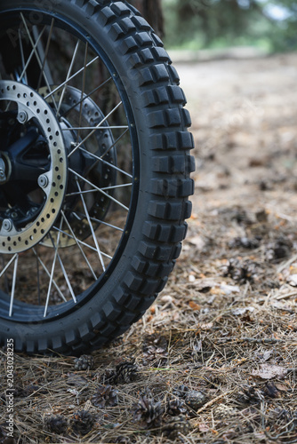 Close-up of knobby off road motorcycle tire and wheel standing on forest ground. Motocross equipment designed for traction and riding on rough terrain.