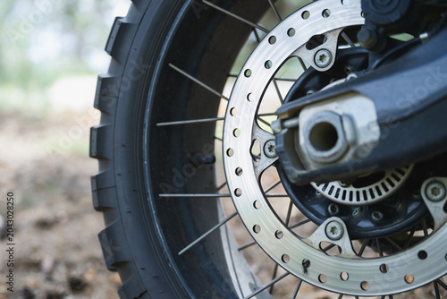 Detailed close-up of motorcycle wheel with brake disc, spokes and knobby off road tire. Technical view of enduro bike components designed for challenging terrain.