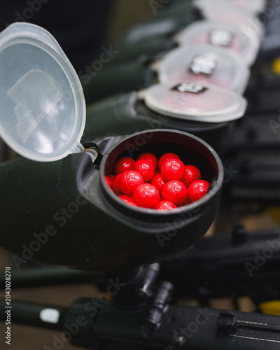 Close-up of paintball marker hopper filled with red paintballs before outdoor game. Recreational shooting equipment prepared for team competition and tactical sport activities.