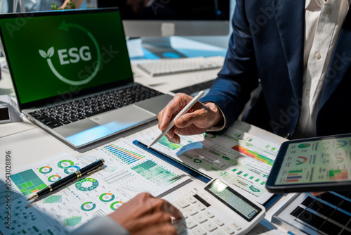 Schilderij op canvas Business team reviews esg reports and green finance charts at office desk with laptop, tablet and calculator, showing sustainability planning, audit work and corporate reporting