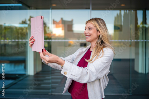 Smiling woman enjoying videocall using pink tablet outdoors