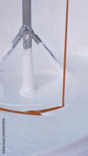Mixer tool enters white paint in bucket, rotating to achieve smooth consistency. Prepare paint for application on walls or surfaces during home renovation or new building construction