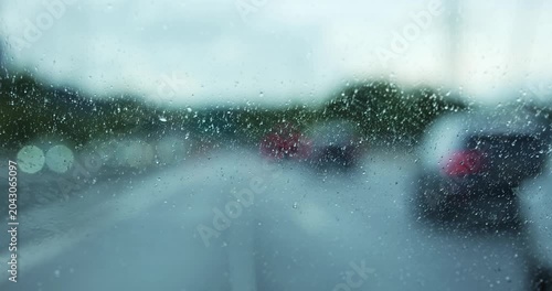 Point of view shot looking through a dirty and smudged car windshield in heavy rain, showing a blurry, shallow depth of field bokeh view of highway traffic tail lights on a rainy day
