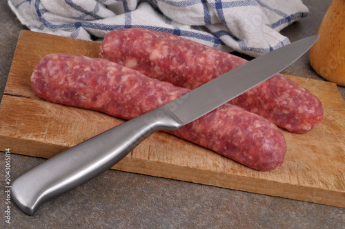 Saucisses de Toulouse crues sur une planche à découper en bois avec un couteau en gros plan sur fond gris